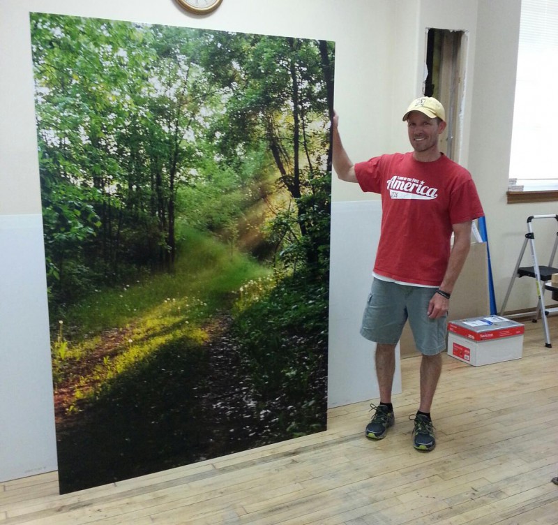 Man standing beside a large forest photo print